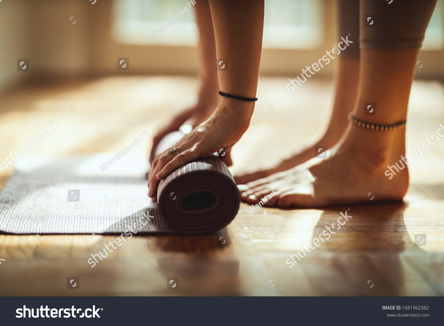 Close up of a womans hands is rolling up exercise mat and preparing to doing yoga. She is exercising on floor mat in morning sunshine at home. #1681962382