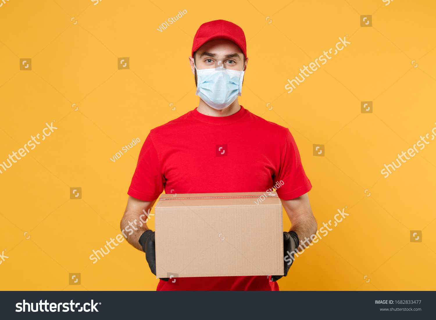 Delivery man employee in red cap blank t-shirt uniform face mask gloves hold empty cardboard box isolated on yellow background studio Service quarantine pandemic coronavirus virus 2019-ncov concept #1682833477
