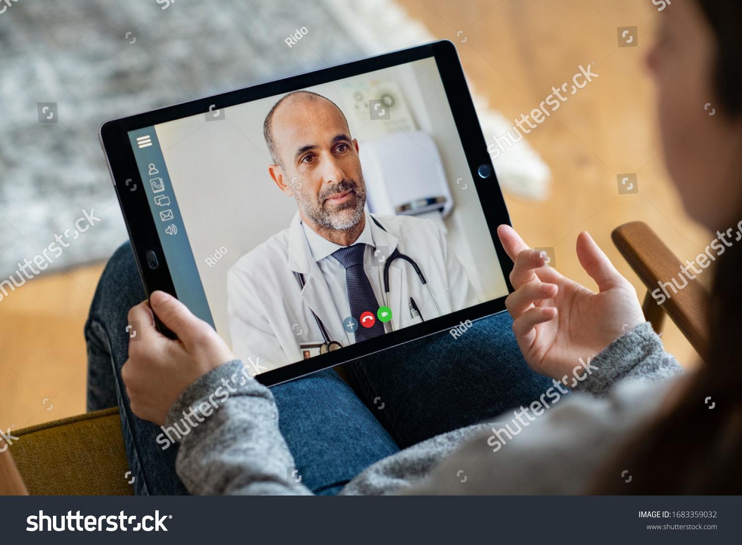 Back view of woman making video call with her doctor while staying at home. Close up of patient in video conferencing with general practitioner on digital tablet. Sick girl in online consultation. #1683359032