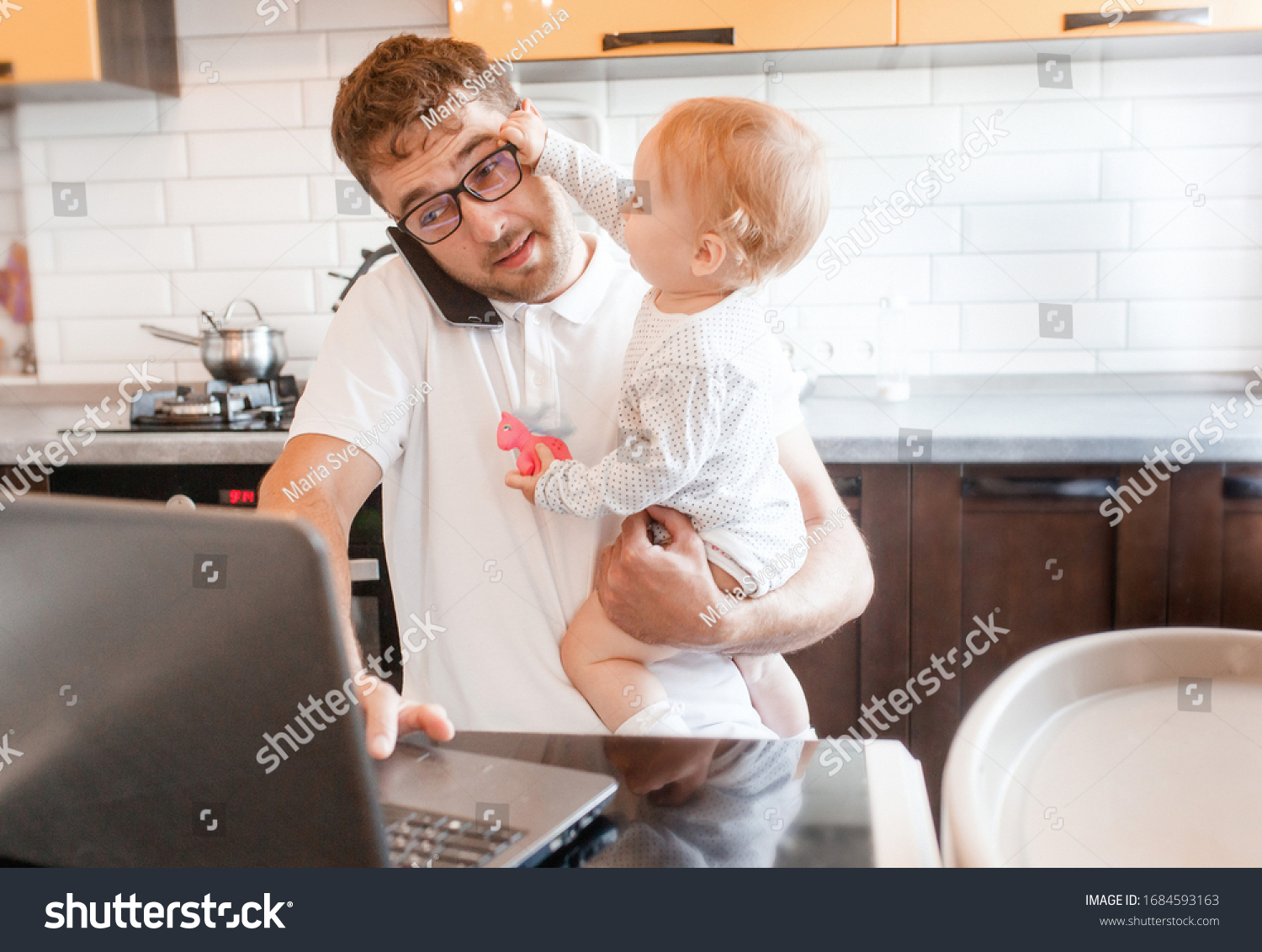 Handsome young man working at home with a laptop with a baby on his hands. Stay home concept. Home office with kids.  #1684593163