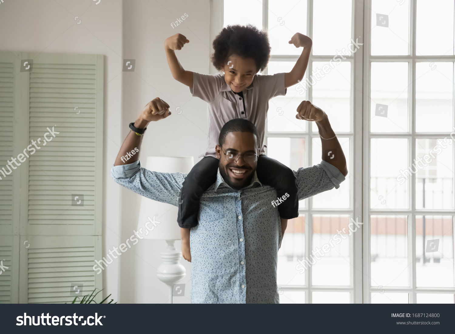 Small son sit on strong dad shoulders showing biceps. African family enjoy activity games at home, healthy fit lifestyle, two superheroes, vitamins for adults and children ad, happy Father Day concept #1687124800