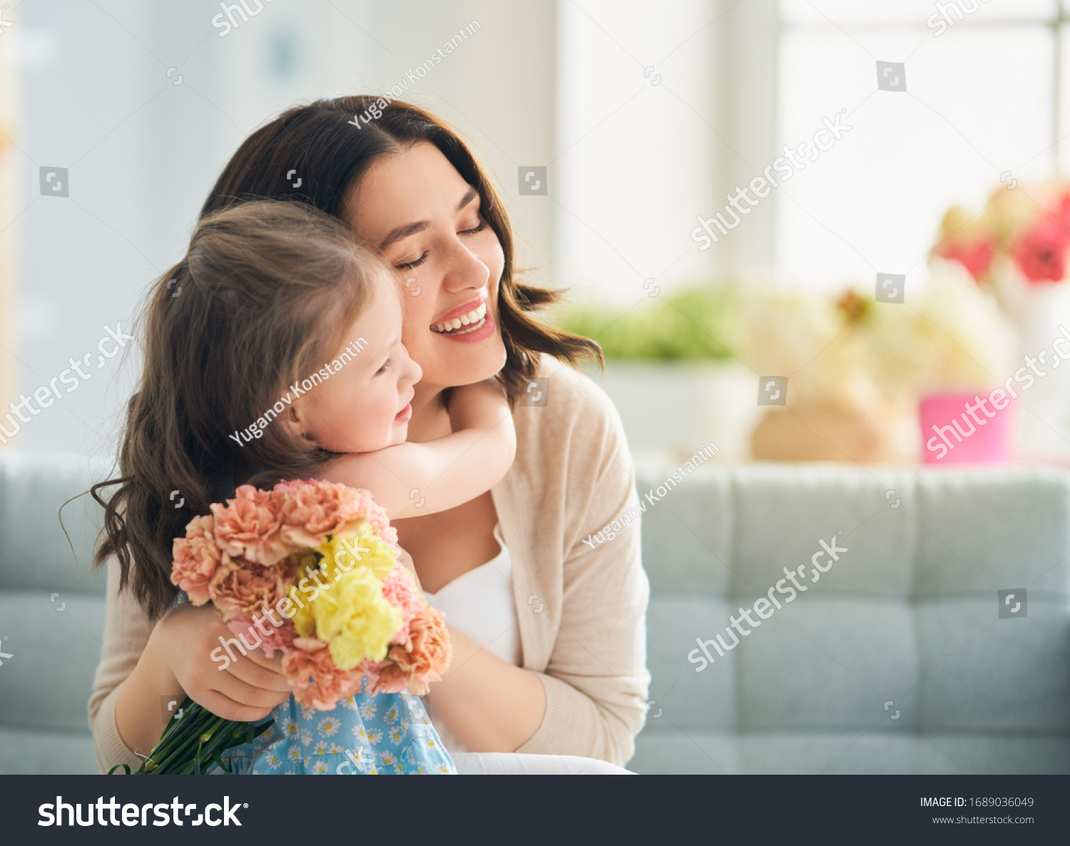 Happy mother's day! Child daughter congratulates mom and gives her flowers. Mum and girl smiling and hugging. Family holiday and togetherness.                                #1689036049