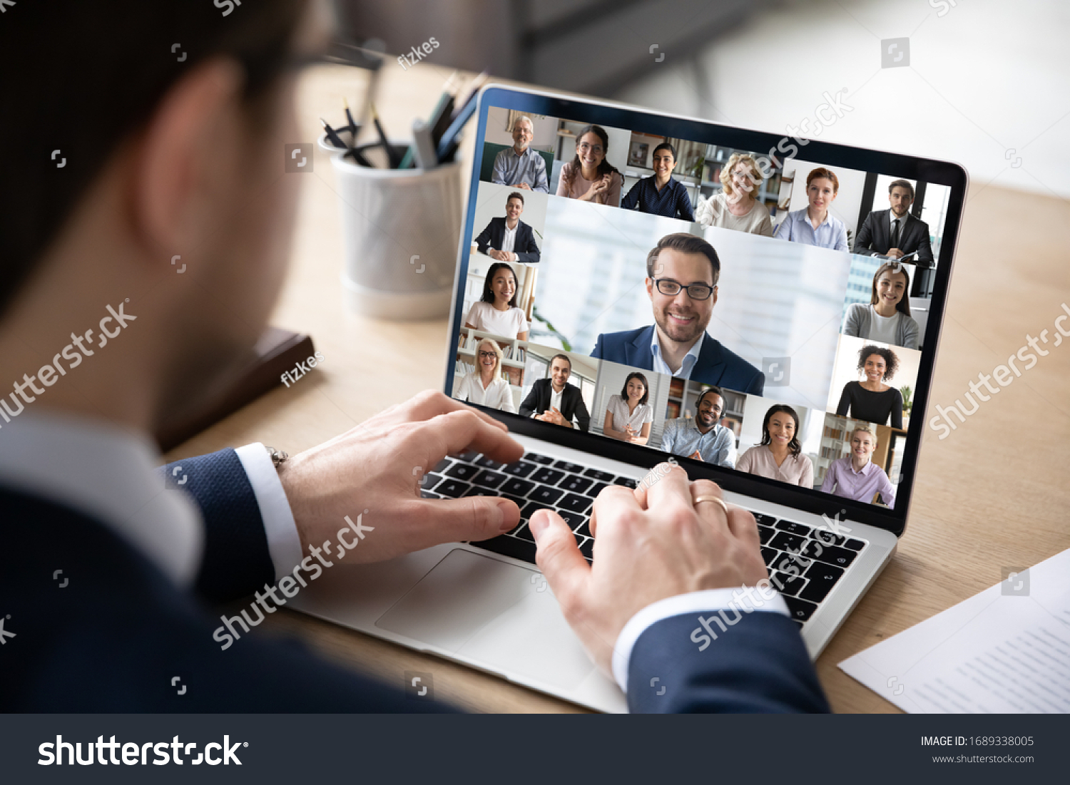 Rear view of businessman speak on web conference with diverse colleagues using laptop Webcam, male employee talk on video call with multiracial coworkers have online meeting briefing from home #1689338005