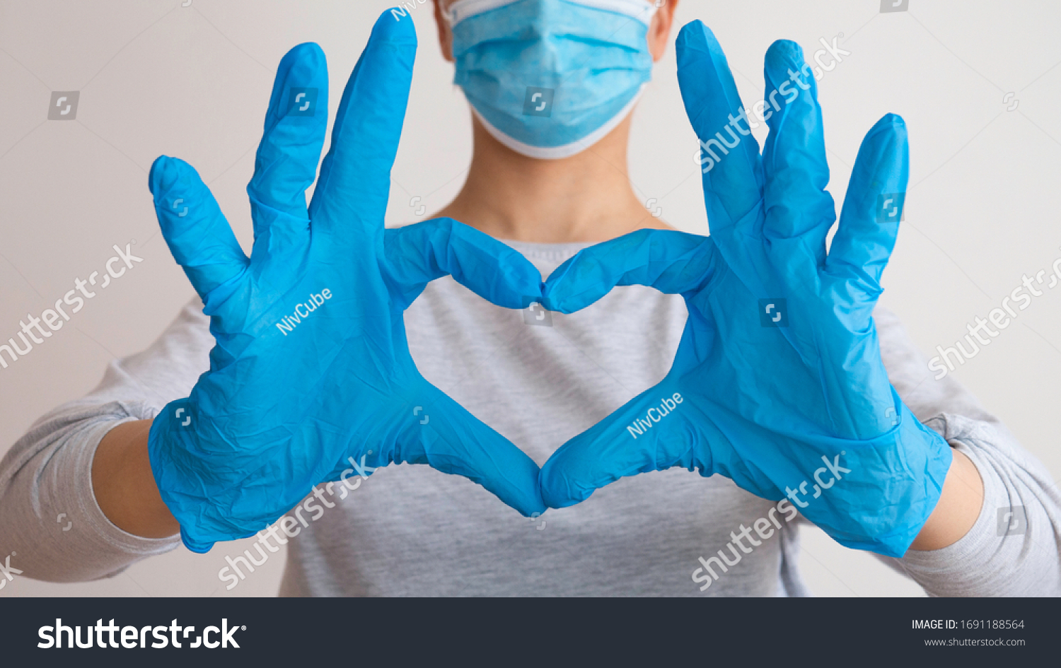 Woman with a medical mask and hands in latex glove shows the symbol of the heart. Doctor for the heart. Love to our pancreas. Love our medical professionals. #1691188564