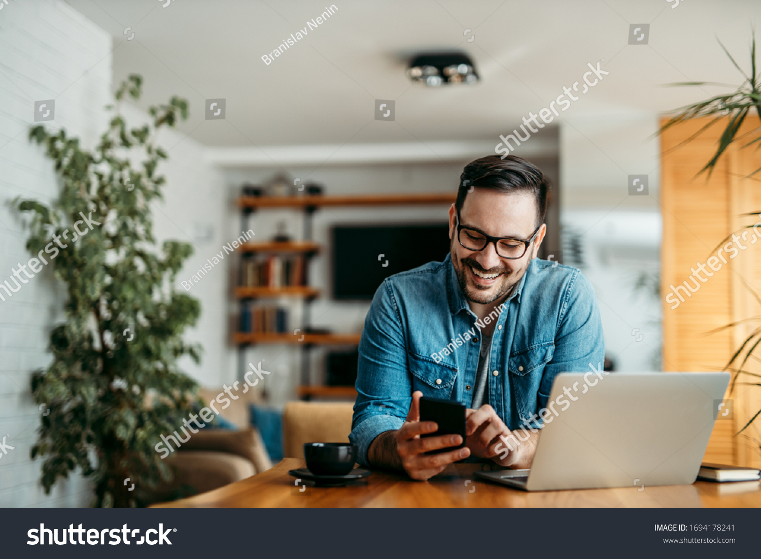 Portrait of a cheerful man using smart phone at home office. #1694178241