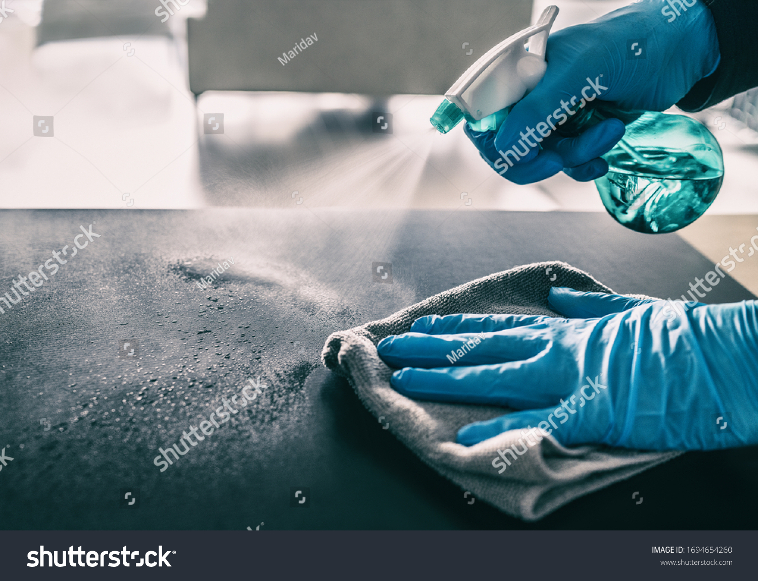 Surface sanitizing against COVID-19 outbreak. Home cleaning spraying antibacterial spray bottle disinfecting against coronavirus wearing nitrile gloves. Sanitize hospital surfaces prevention. #1694654260