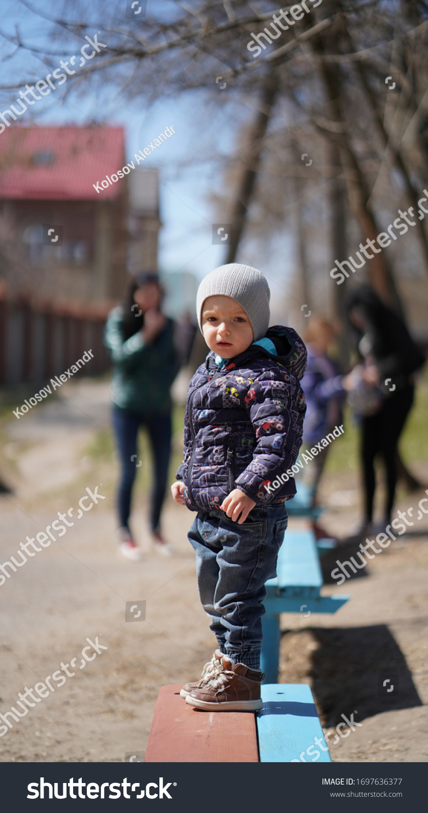 Portrait of little cute boy in a purple jacket and hat in the spring in the park. Child looks away #1697636377
