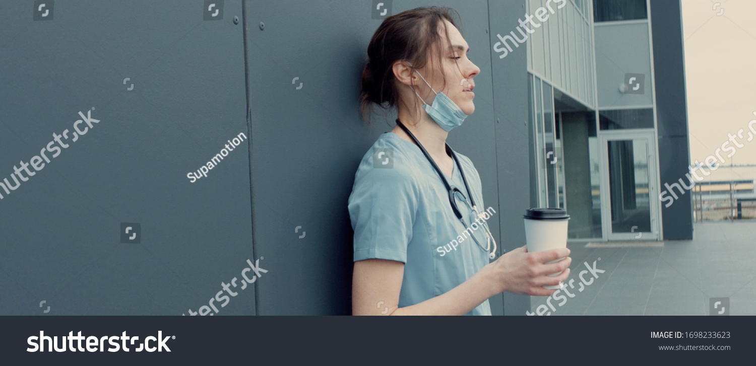 Portrait of tired exhausted nurse or doctor having a coffee break outside in the morning. COVID-19, Coronavirus pandemic #1698233623