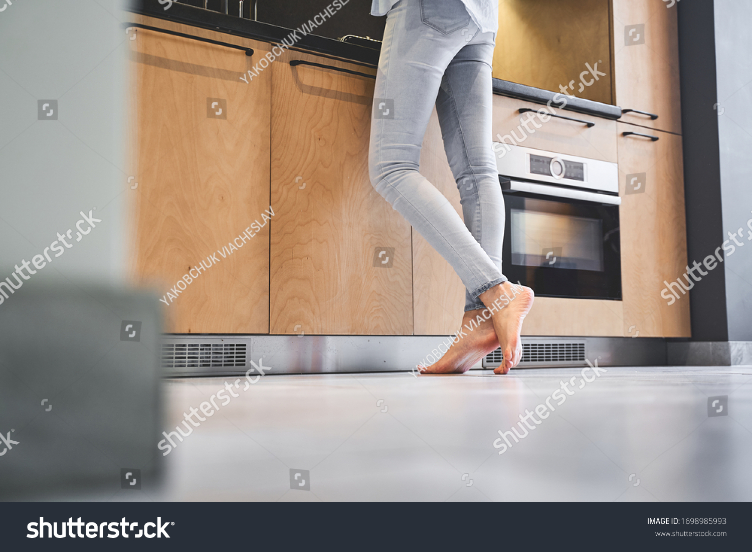 Cropped photo of a young housewife in denim pants standing barefoot on the tile floor #1698985993