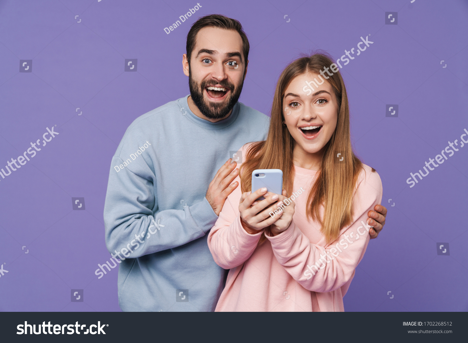 Image of excited surprised loving couple isolated over purple background using mobile phone. #1702268512