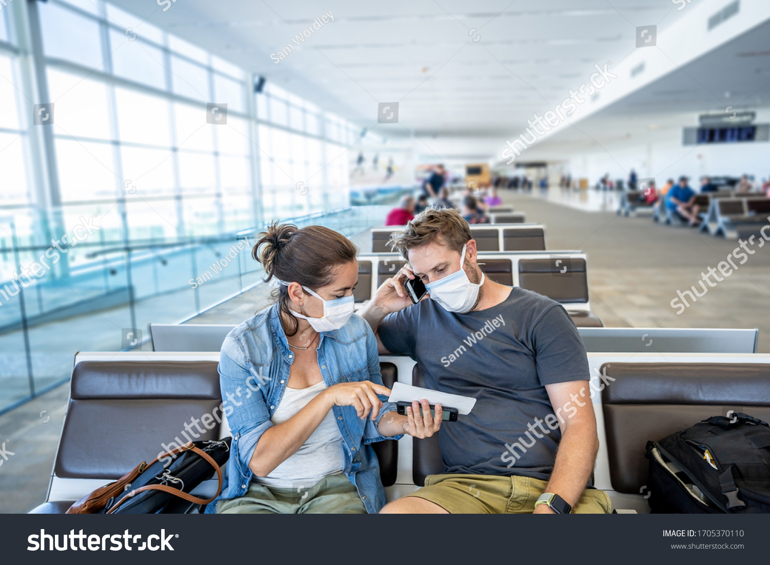 COVID-19 worldwide borders closures. Couple with face mask stuck in airport terminal after being denied entry to other countries. Passengers stranded in airport on his travel back to home country. #1705370110