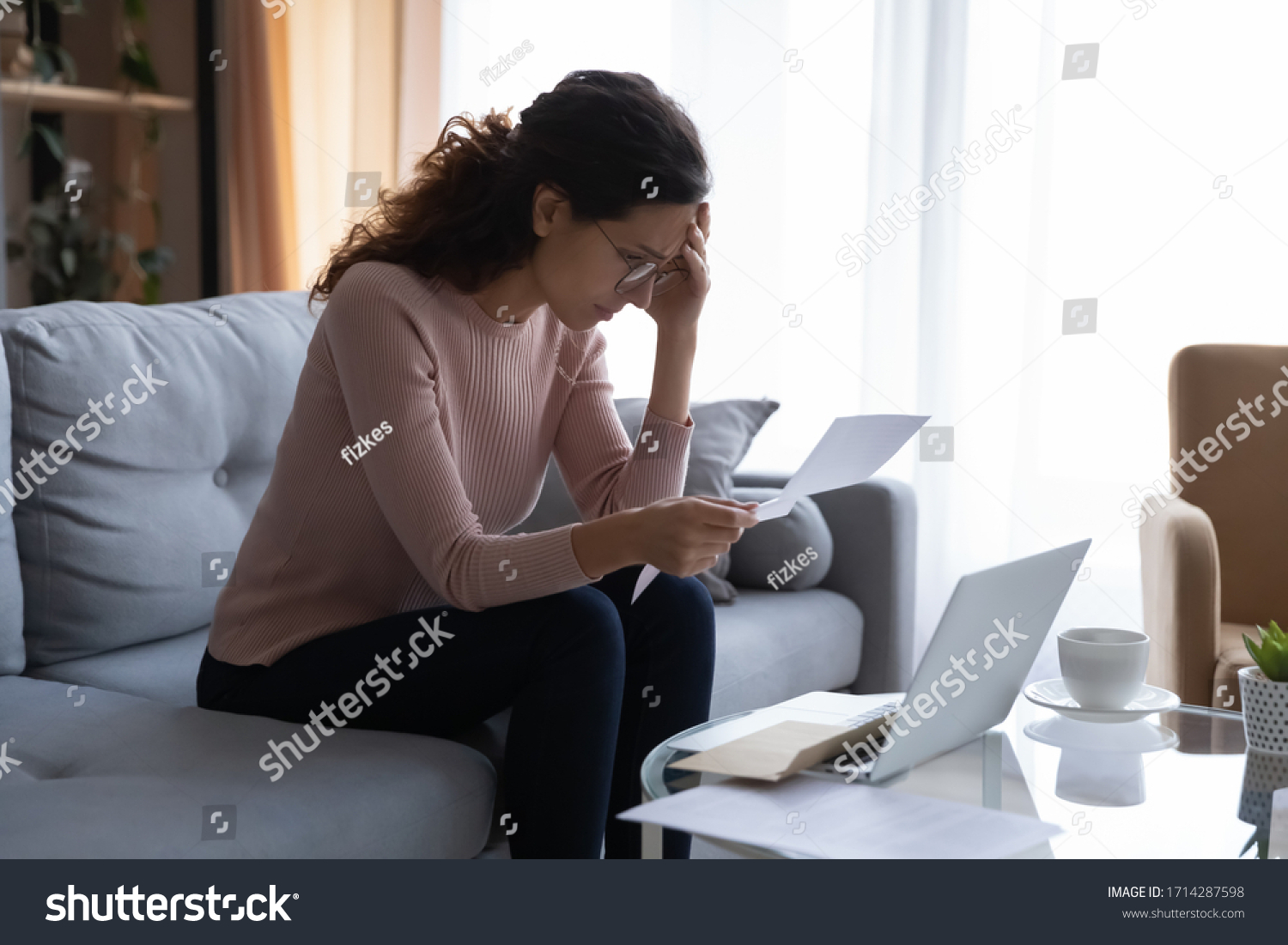 Frustrated desperate young woman in eyeglasses touching forehead, looking through banking credit termination, having financial problems, reading refusal document, feeling depressed alone at home. #1714287598