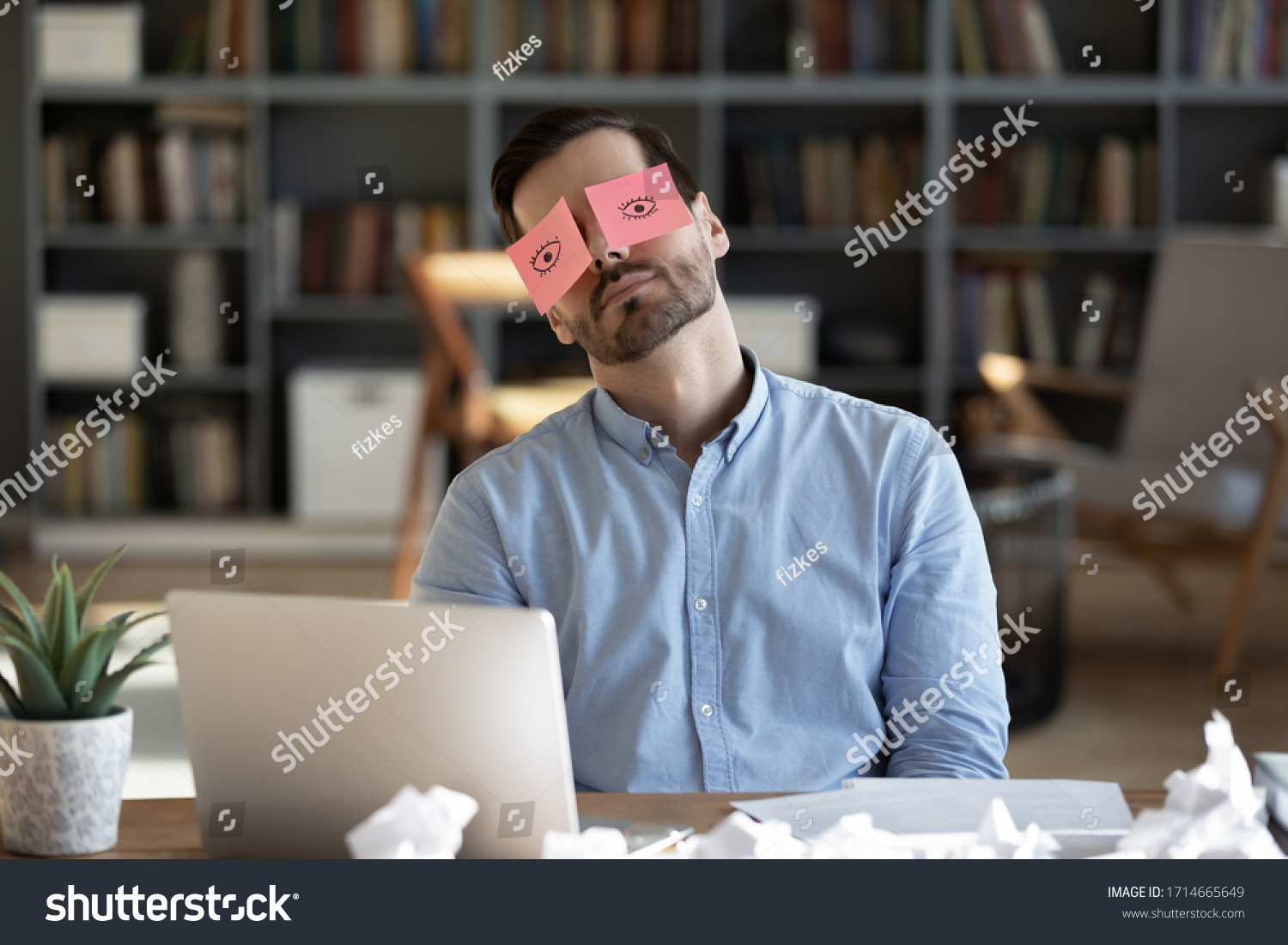 Exhausted tired businessman with painted eyes on stickers, adhesive notes on face sleeping at workplace, sitting at desk with laptop, unproductive lazy young male dozing, working on difficult project #1714665649
