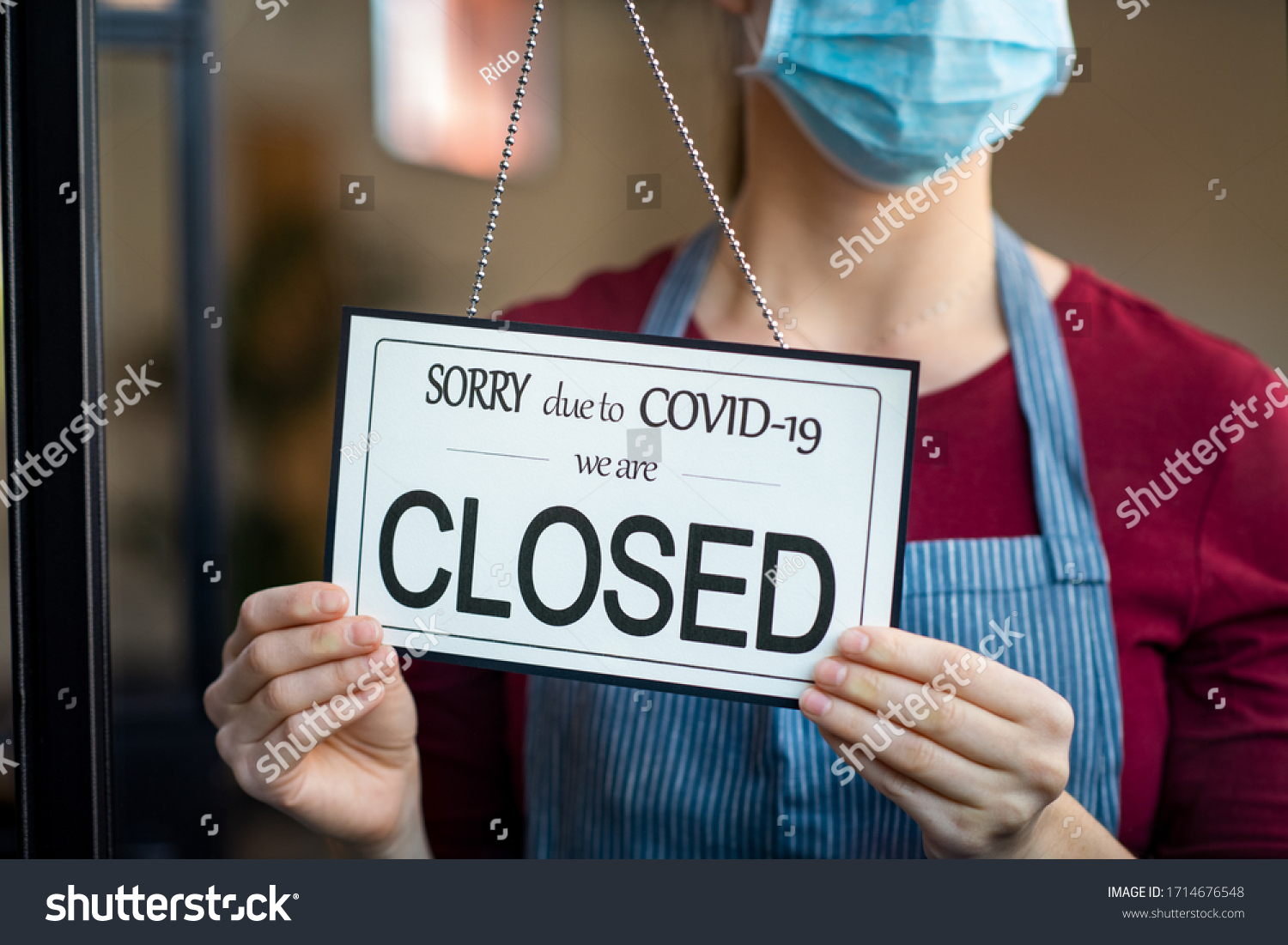 Businesswoman closing her business activity due to covid-19 lockdown. Owner with surgical mask close the doors of her store due to quarantine coronavirus. Close up sign due to the effect of COVID-19. #1714676548