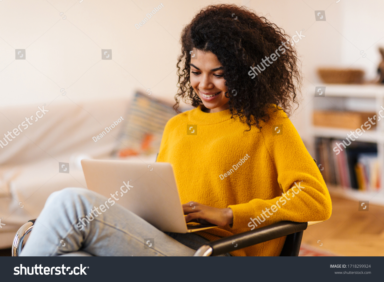 Image of cheerful african american woman using laptop while sitting on chair in living room #1718299924