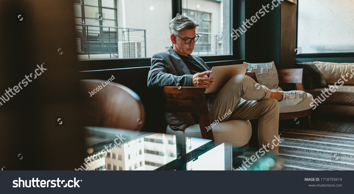 Mature businessman sitting in office lobby with a laptop. Male executive working in office lounge. #1718759419