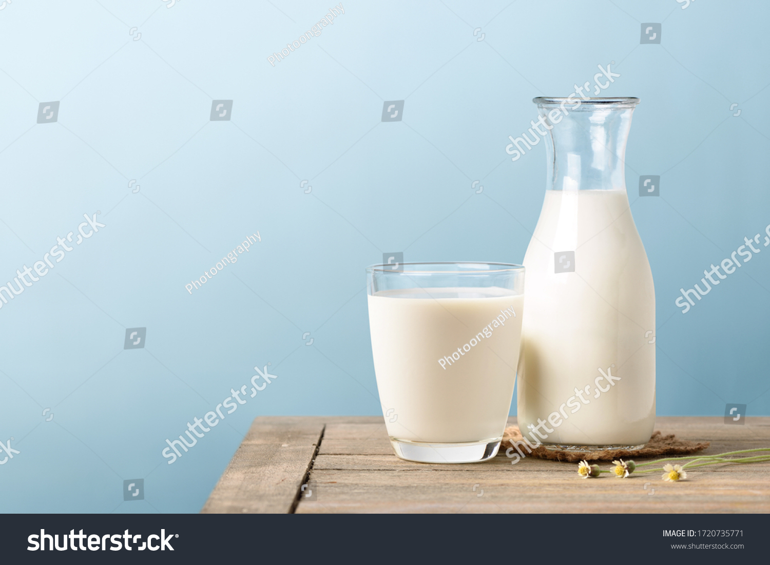 A glass and bottle of milk on wooden table with light blue background. #1720735771