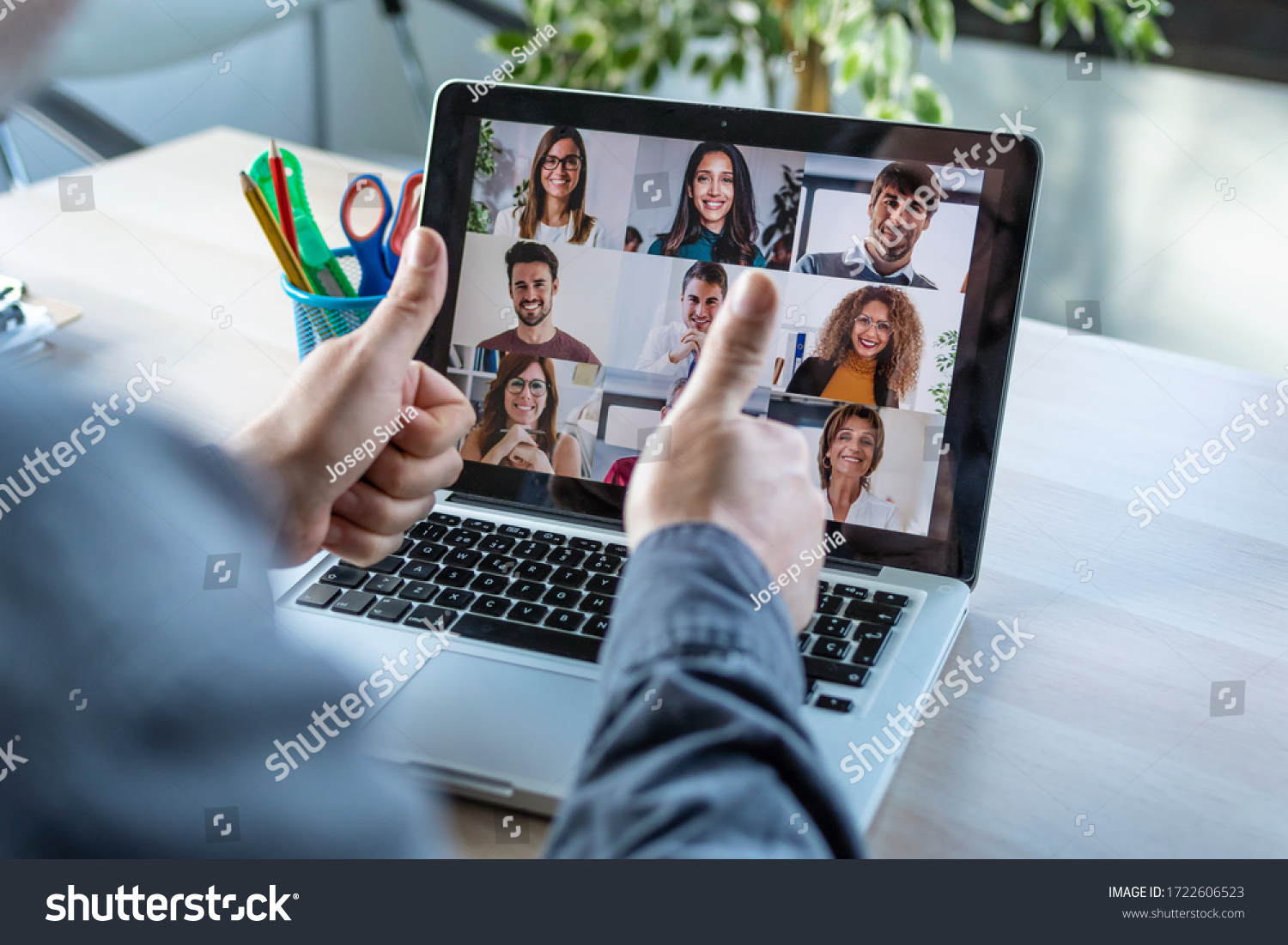 Back view of male employee making a gesturing approval with thumb fingers while speak on video call with diverse colleagues on online briefing with laptop at home. #1722606523