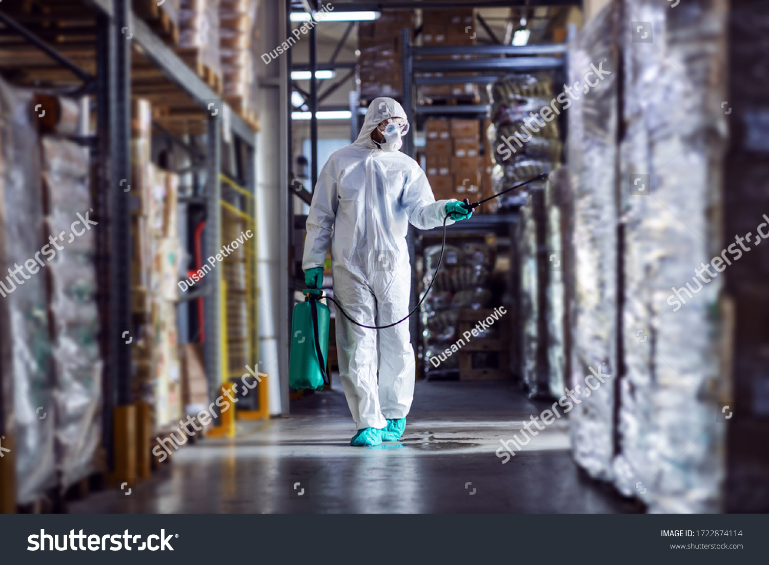 Man in protective suit and mask disinfecting warehouse full of food products from corona virus / covid-19. #1722874114