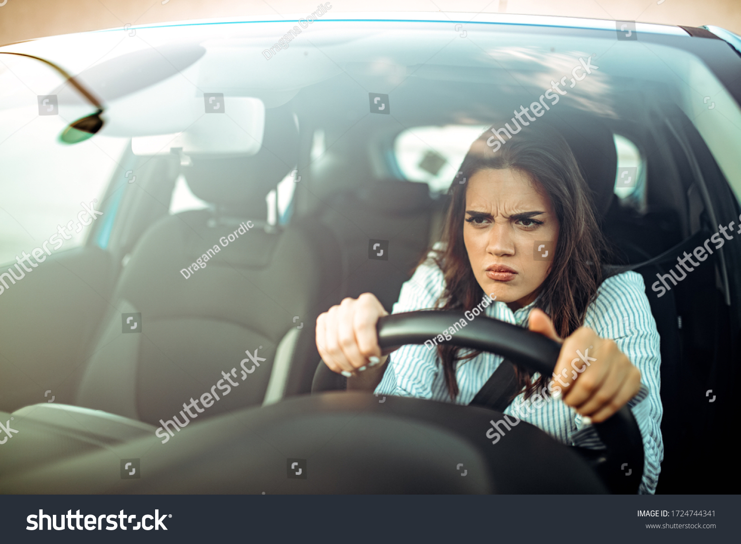 Road rage! Enraged young woman driver shouts and points accusingly.  Profile of an angry young driver. Negative human emotions face expression. Angry woman driving a car #1724744341