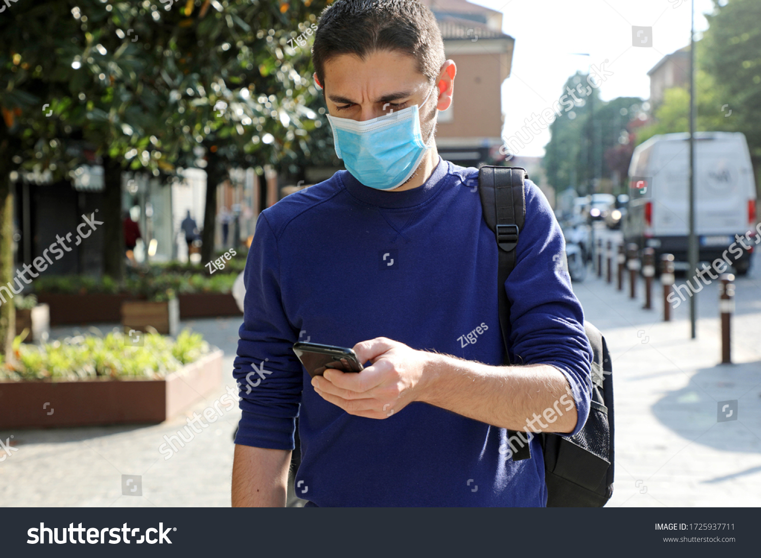COVID-19 Pandemic Coronavirus Worried Young Man Wearing Surgical Mask Using Smart Phone App in City Street to Aid Contact Tracing and Self Diagnostic in Response to the Coronavirus Pandemic 2019 #1725937711