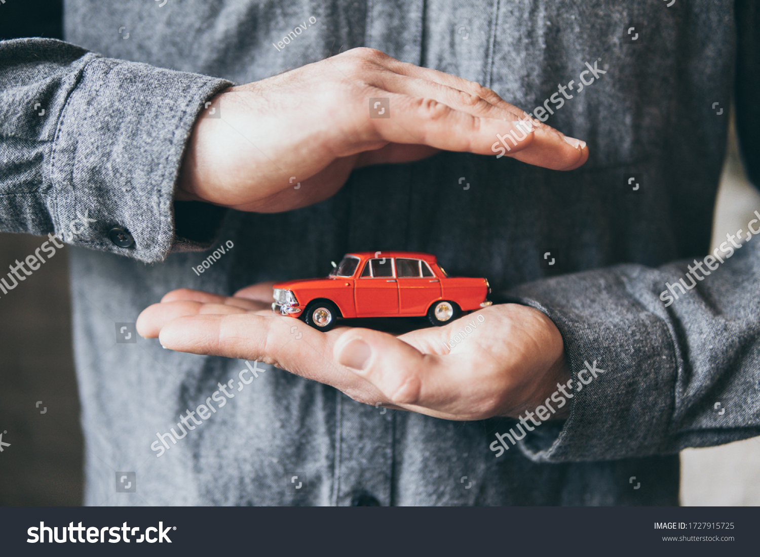 Male hands holding and protecting a red toy car. Conceptual image of insurance and road safety. #1727915725