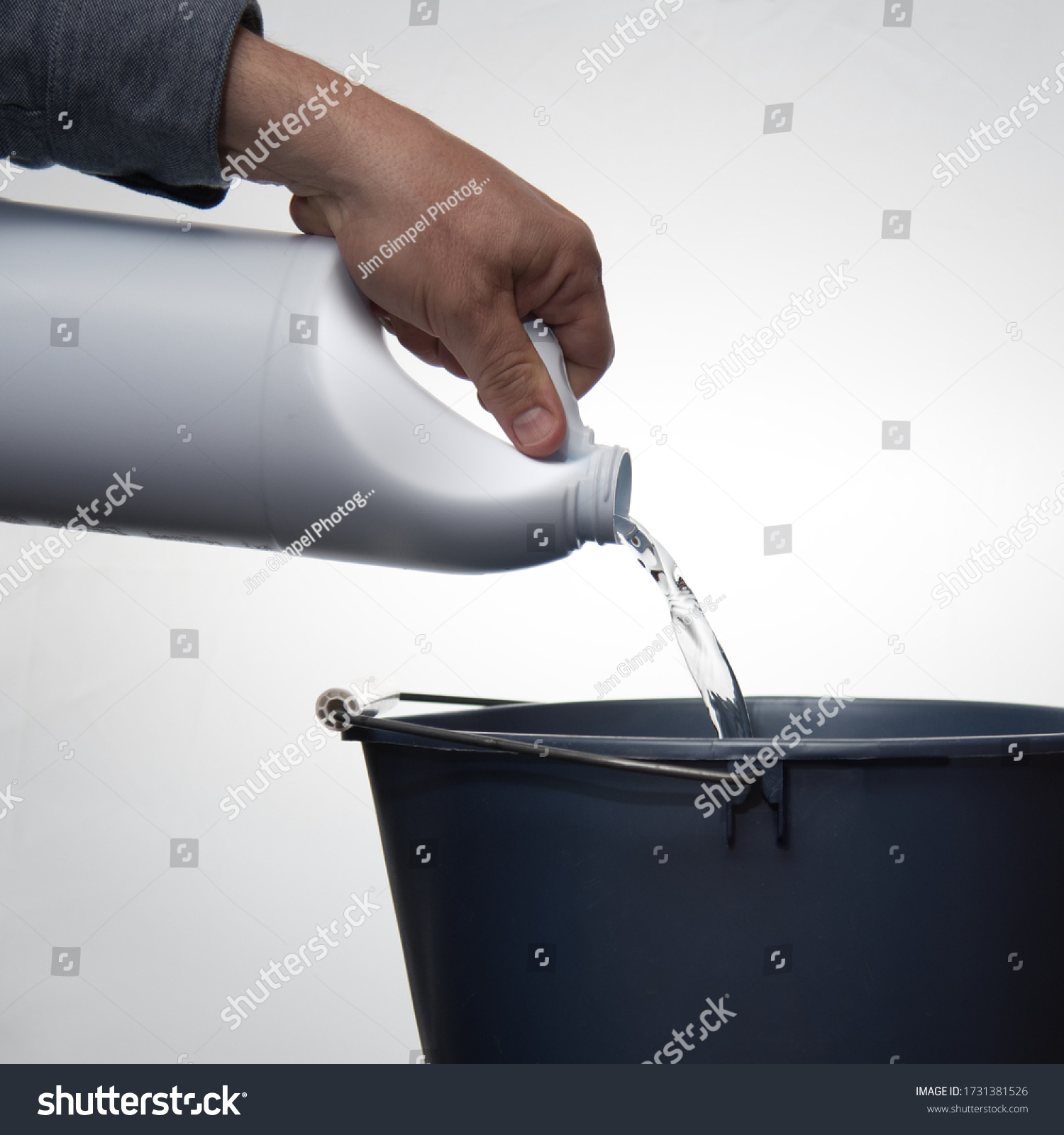 A man's hand pouring cleaner or bleach into a blue bucket against a white background. #1731381526