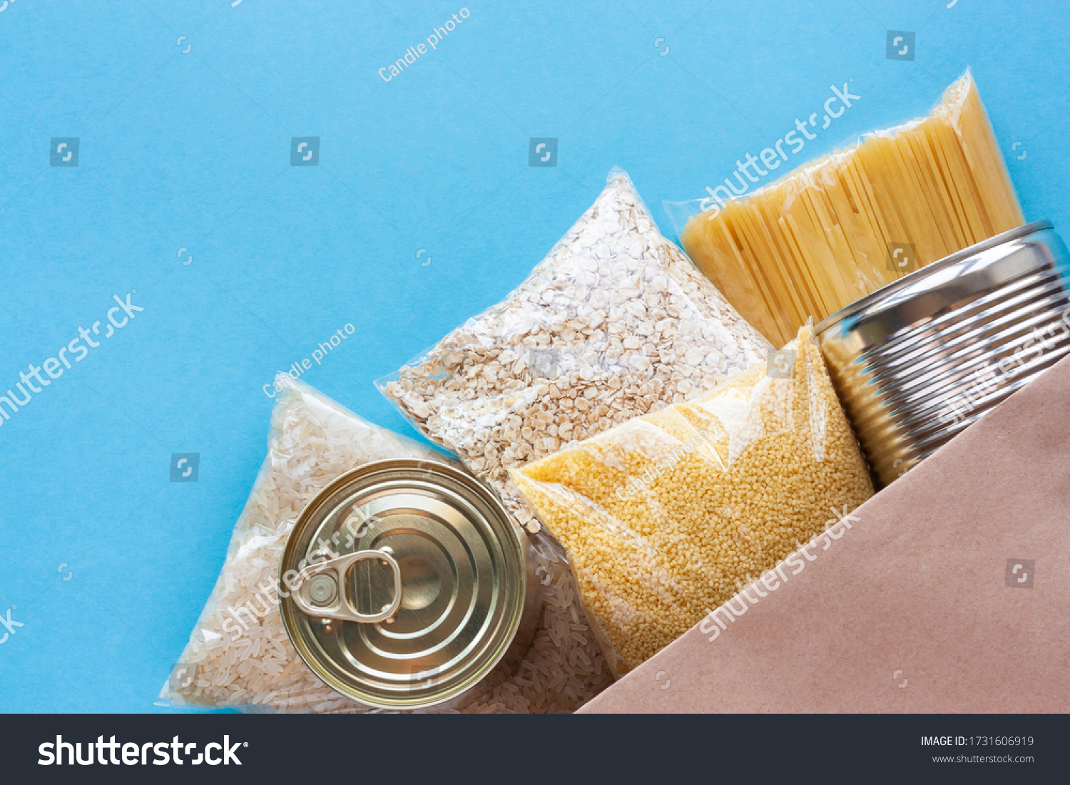 Various grocery products in packages top view. Pasta, cereals and canned food in paper bag on blue background. Food delivery, donation or stock provision concept. Copy space. #1731606919