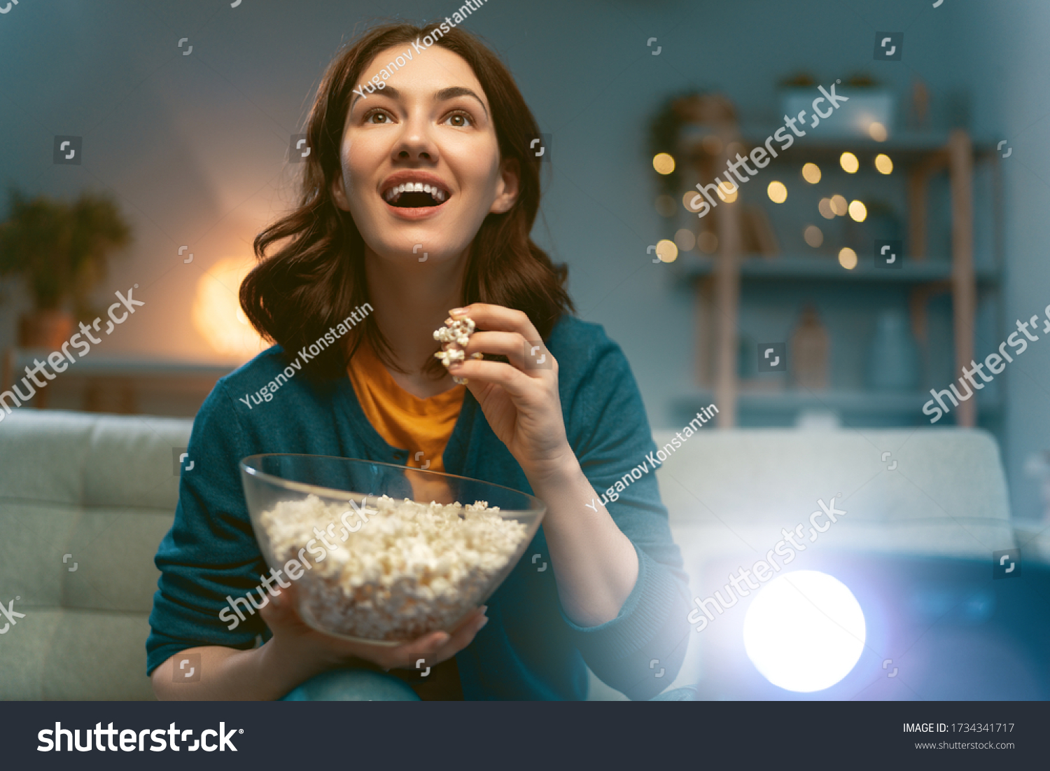 Young woman watching projector, TV, movies with popcorn in the evening. Girl spending time at home. #1734341717