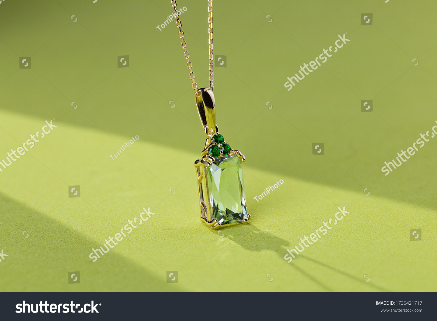 Elegance gold pendant necklace with baguette cut beryl gem and emeralds on bright green background. Fashion jewelry with natural gemstone #1735421717