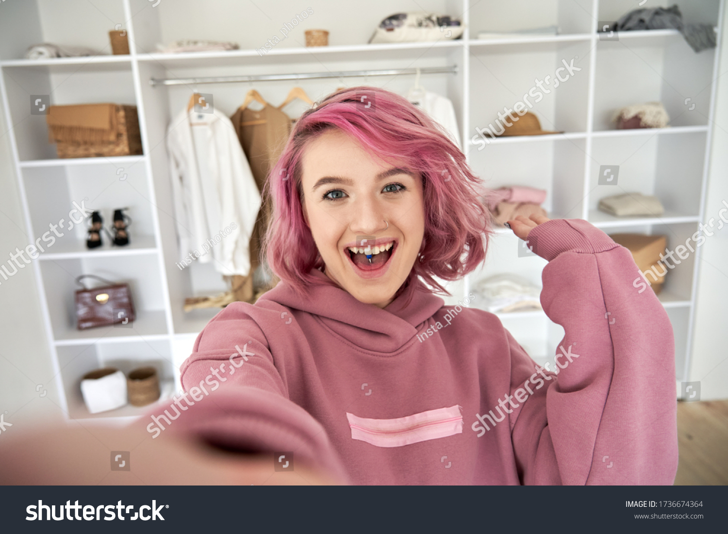 Excited hipster gen z teen girl fashion social media channel blogger stylist with pink hair piercing wear hoodie look at camera record vlog video tutorial in front of clothes wardrobe, face headshot. #1736674364