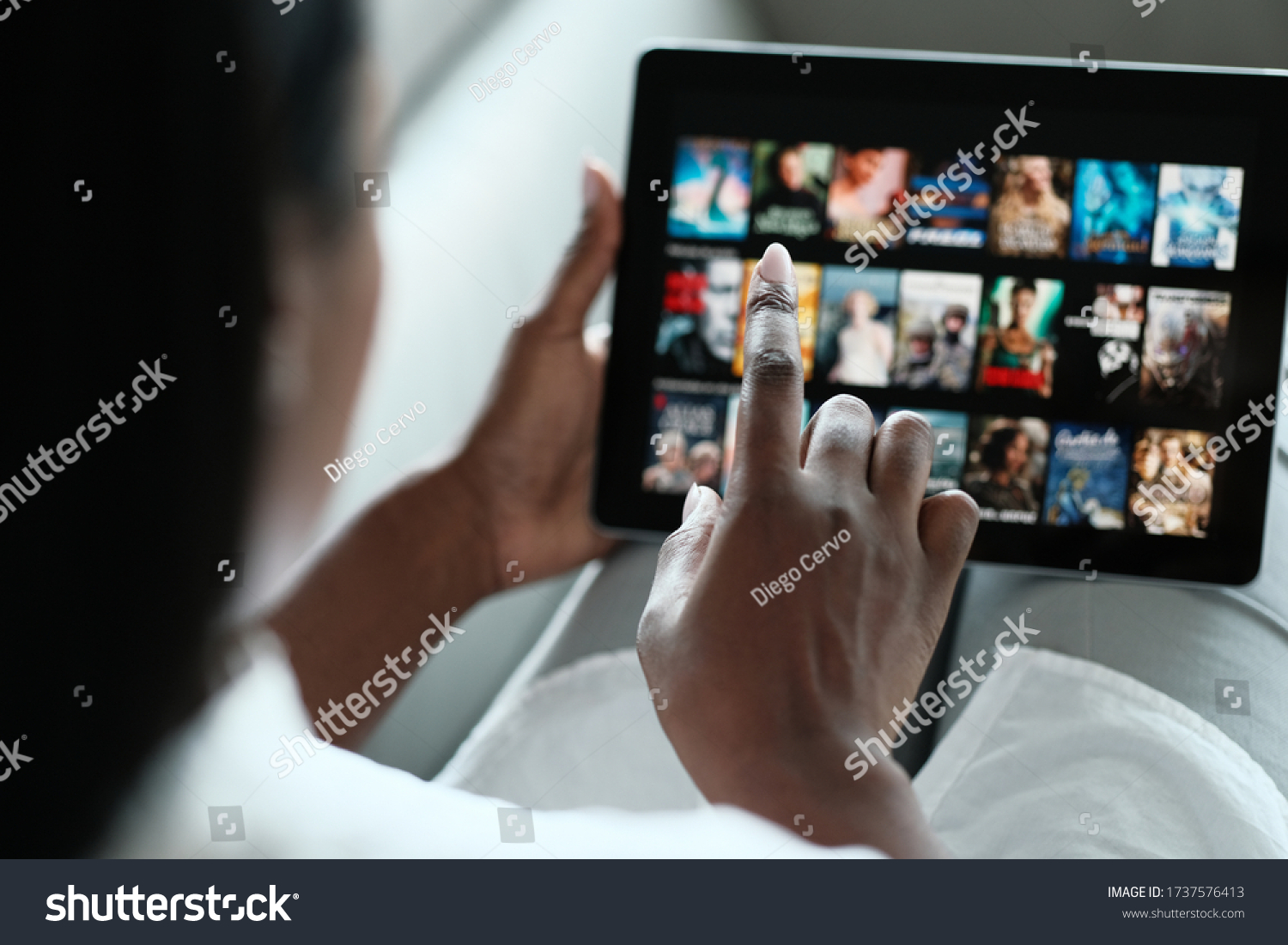 African American Woman Lying Down On Sofa At Home, Choosing Movie On Internet Streaming Service. Over The Shoulders. #1737576413