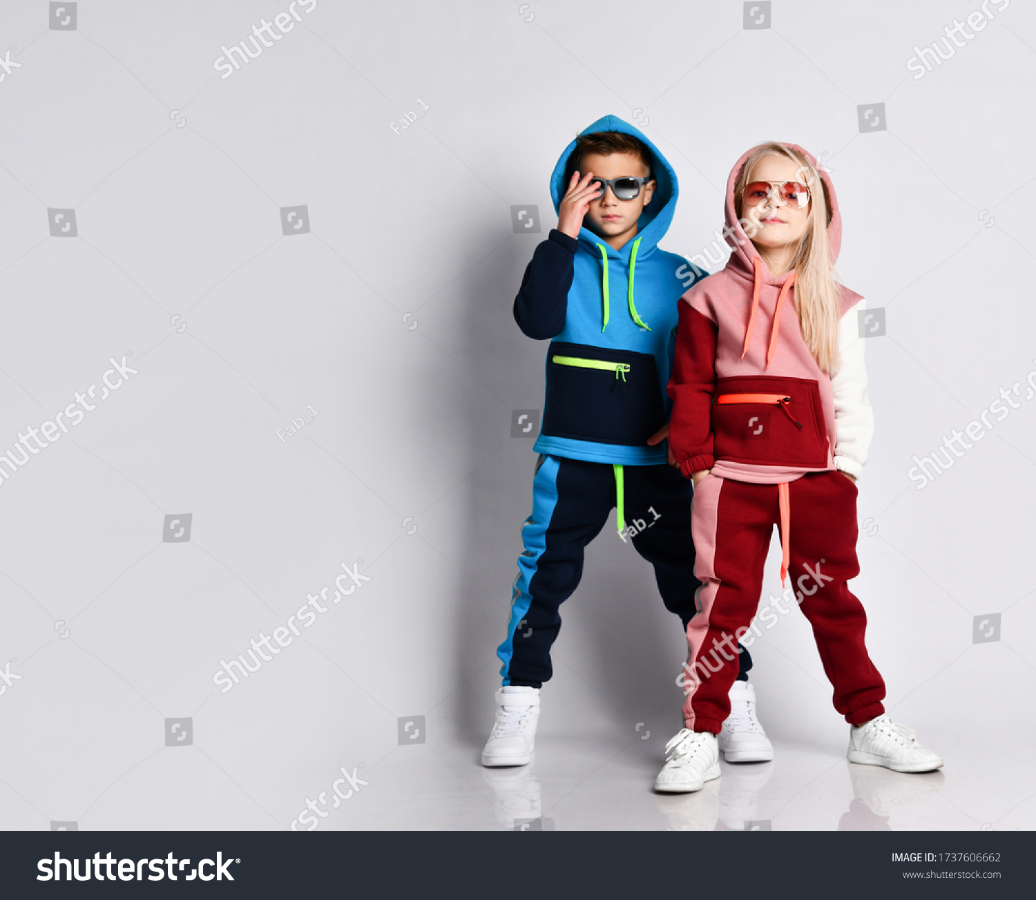 Little kids, boy and girl, in sunglasses and hoods, colorful tracksuits, sneakers. They posing isolated on white studio background. Childhood, fashion, advertising and sport. Full length, copy space #1737606662