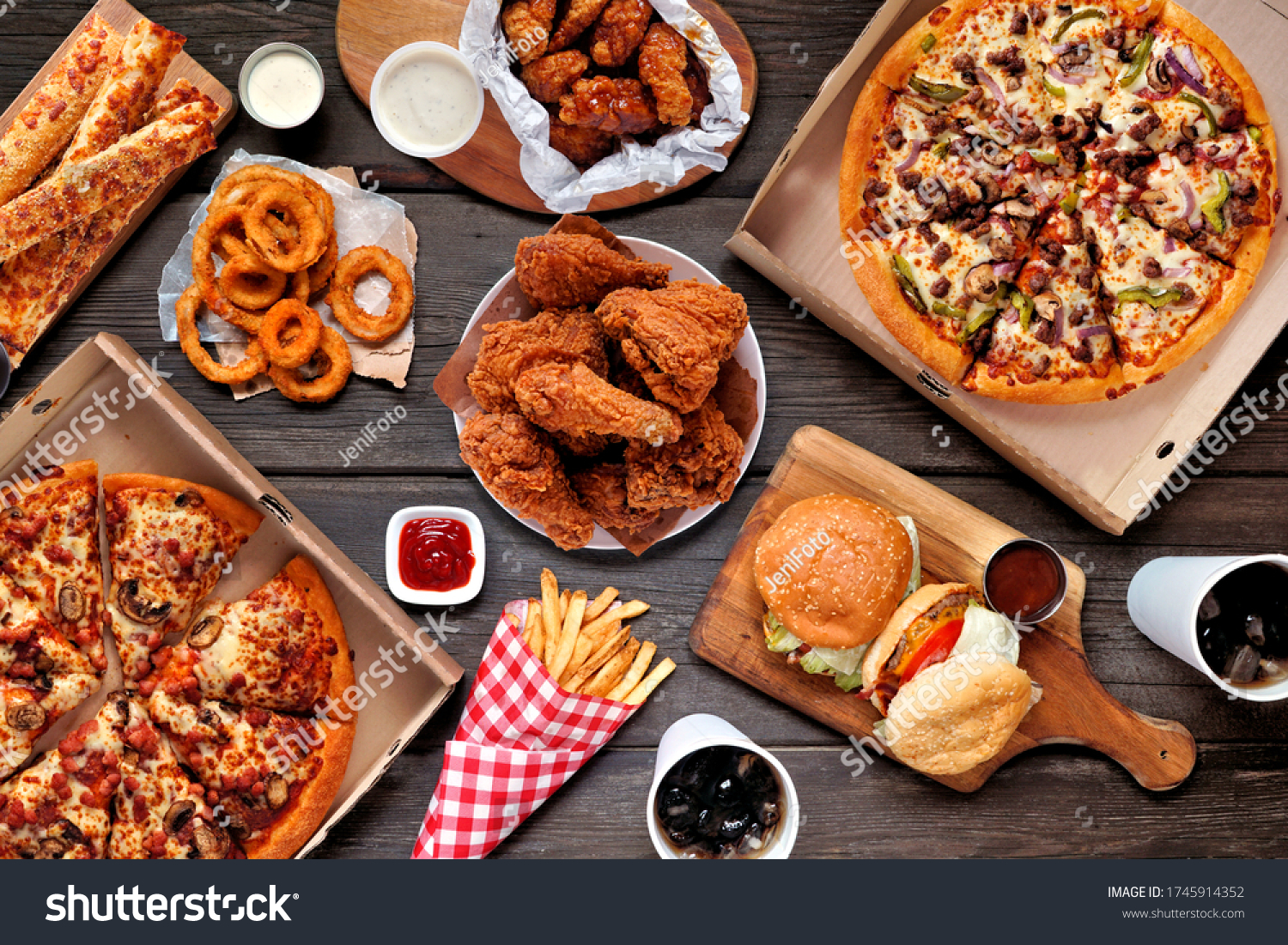 Buffet table scene of take out or delivery foods. Pizza, hamburgers, fried chicken and sides. Above view on a dark wood background. #1745914352