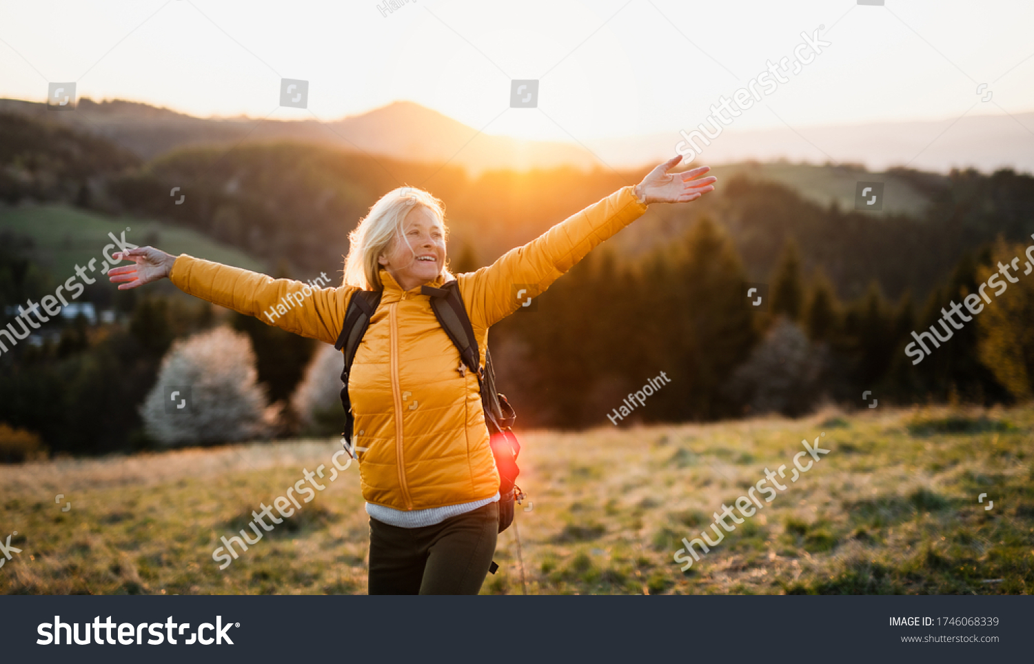 Front view of senior woman hiker standing outdoors in nature at sunset. #1746068339
