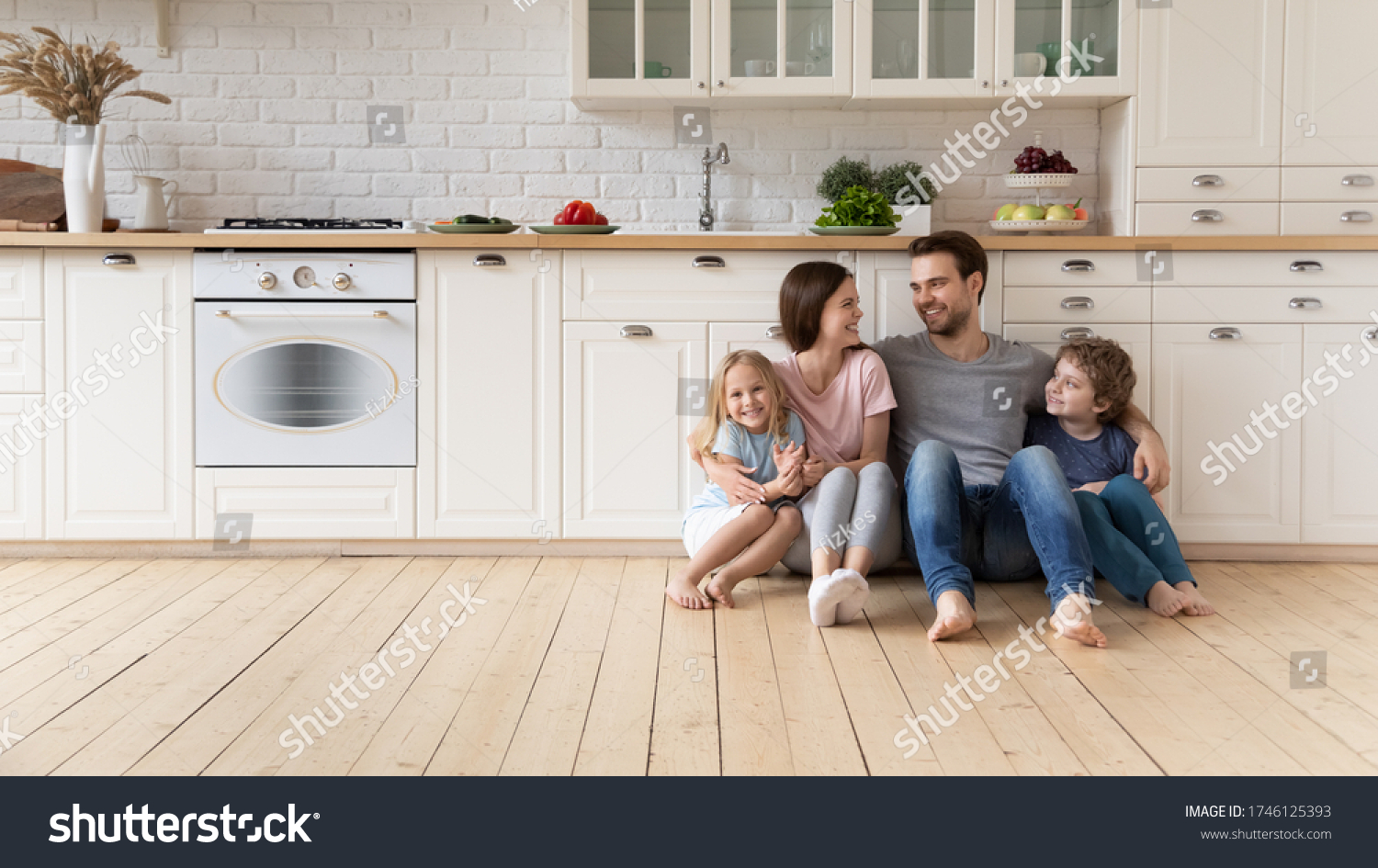 Happy young family with little children sit on warm wooden floor in new modern design kitchen, overjoyed parents with excited small kids relax rest in own renovated apartment, moving concept #1746125393
