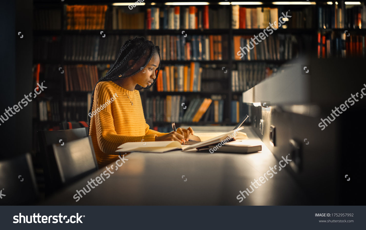 University Library: Gifted Black Girl uses Laptop, Writes Notes for the Paper, Essay, Study for Class Assignment. Students Learning, Studying for Exams College. Side View Portrait with Bookshelves #1752957992