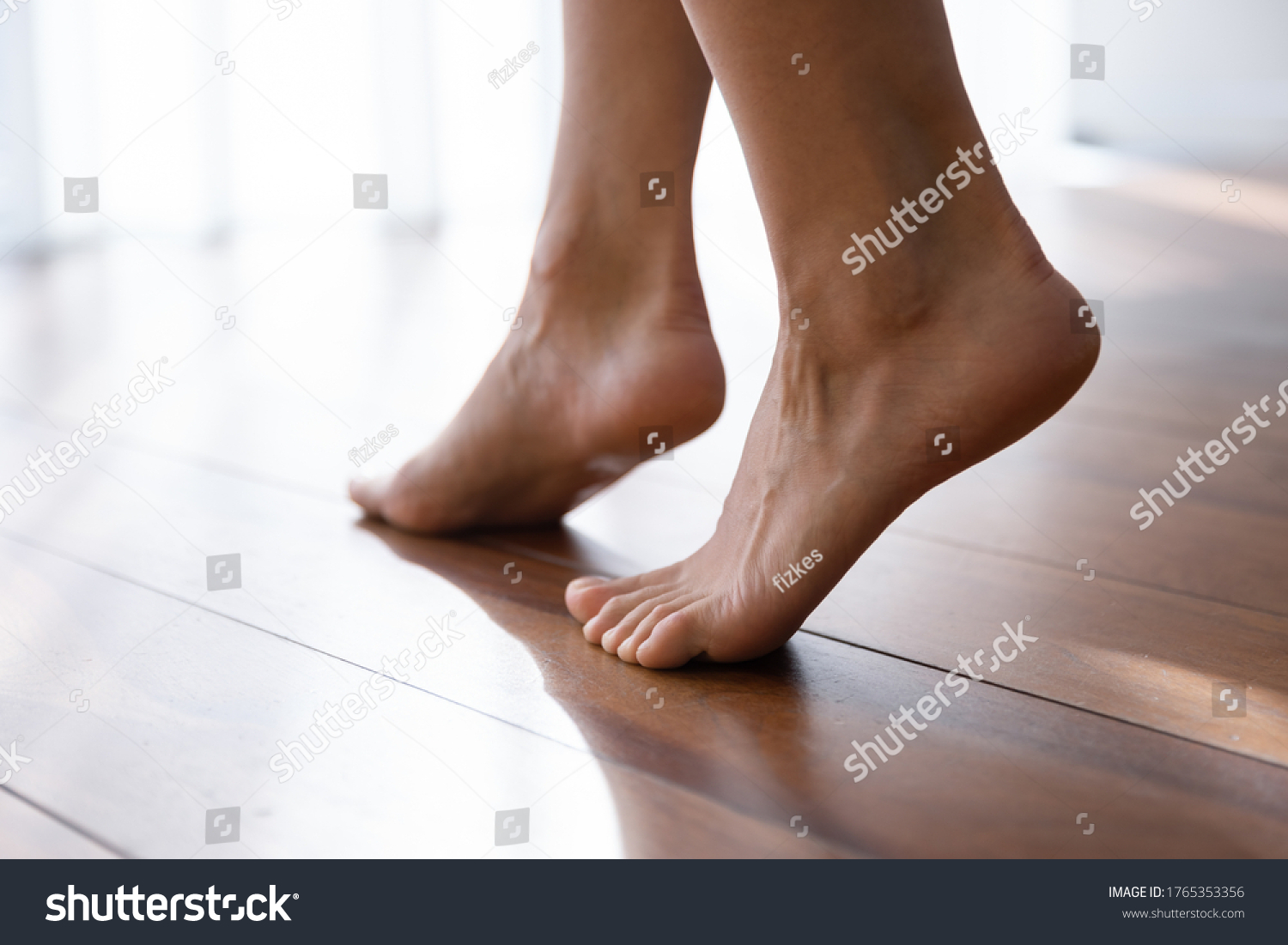 Close up of young female legs step barefoot on warm wooden floor in living room at home or hotel, woman girl walk with soft bare feet in apartment with underfloor electric heating #1765353356