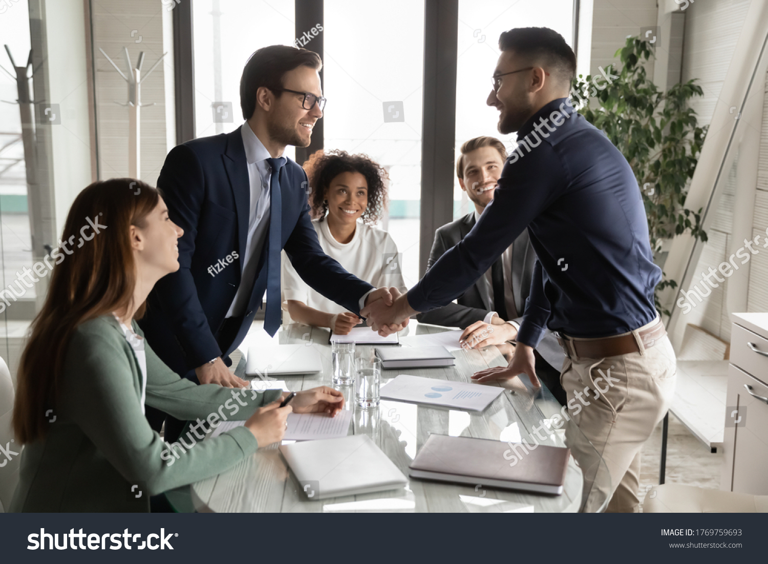Smiling multiethnic male business partners shake hands close deal make agreement at team meeting in boardroom, excited diverse businessmen handshake get acquainted greeting at briefing in office #1769759693