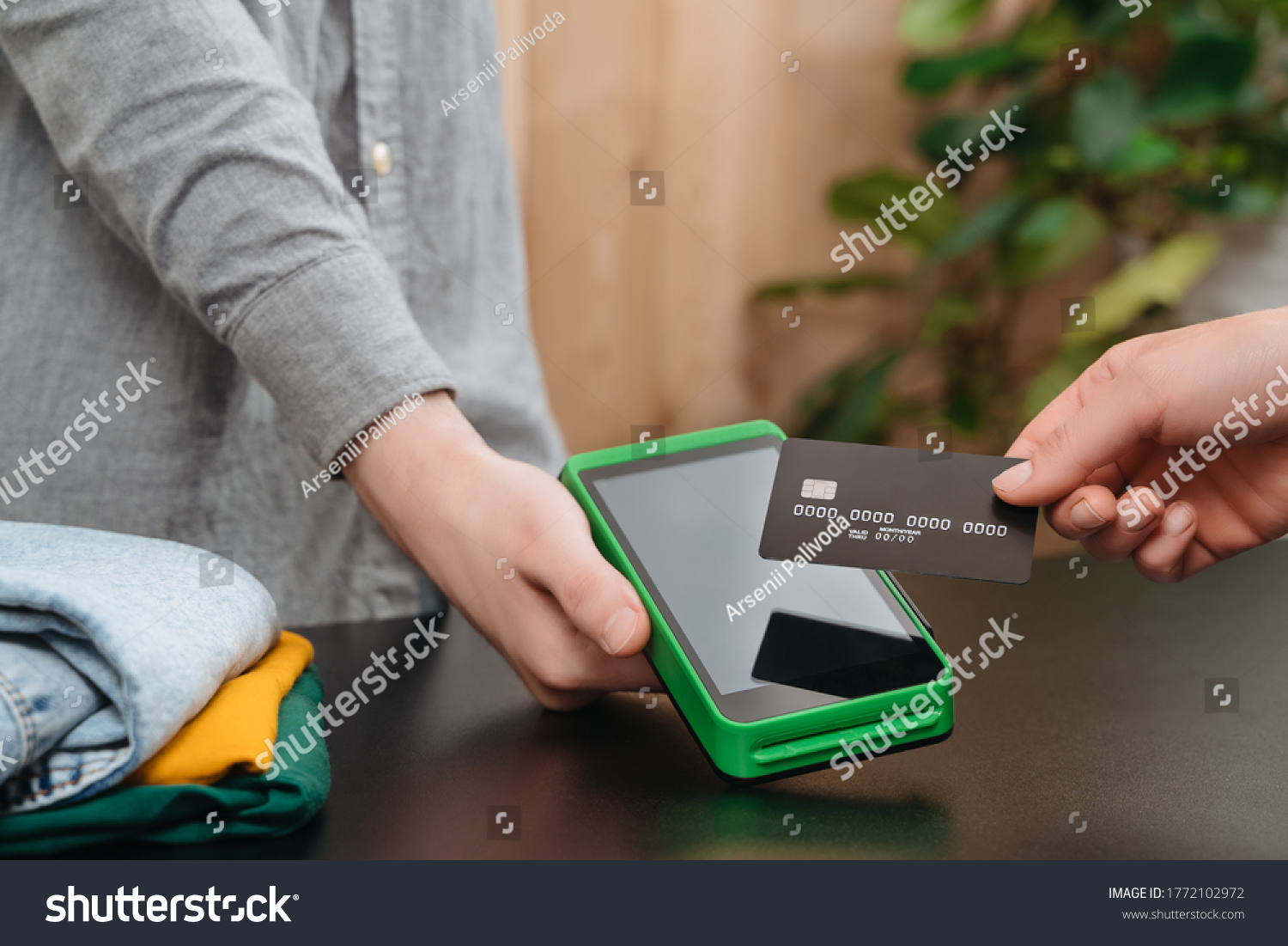 Client's hand holding bank credit card near nfc payment terminal in hand of cashier in clothing store. Customer makes purchases with credit card. Contactless, mobile, express payment, nfc concept  #1772102972