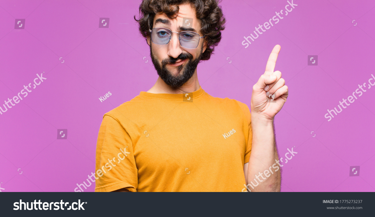 young crazy cool man feeling like a genius holding finger proudly up in the air after realizing a great idea, saying eureka against flat wall #1775273237