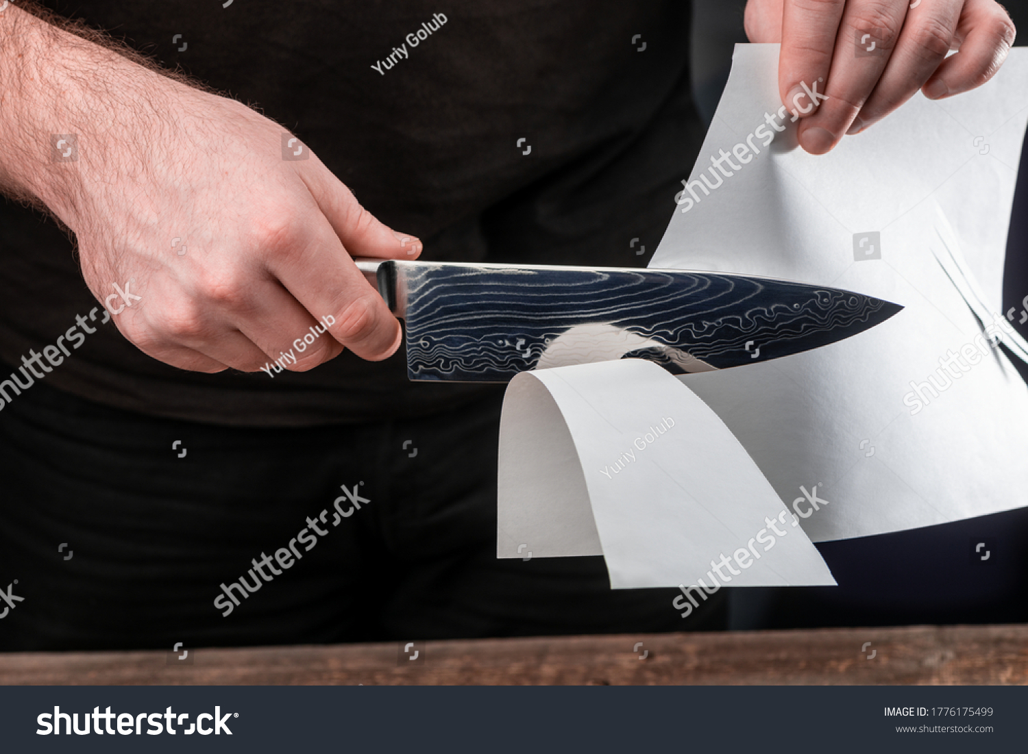 Man testing sharpness of knife by cutting a thin sheet of paper. Japanese Gyuto knife with Damascus steel blade. #1776175499