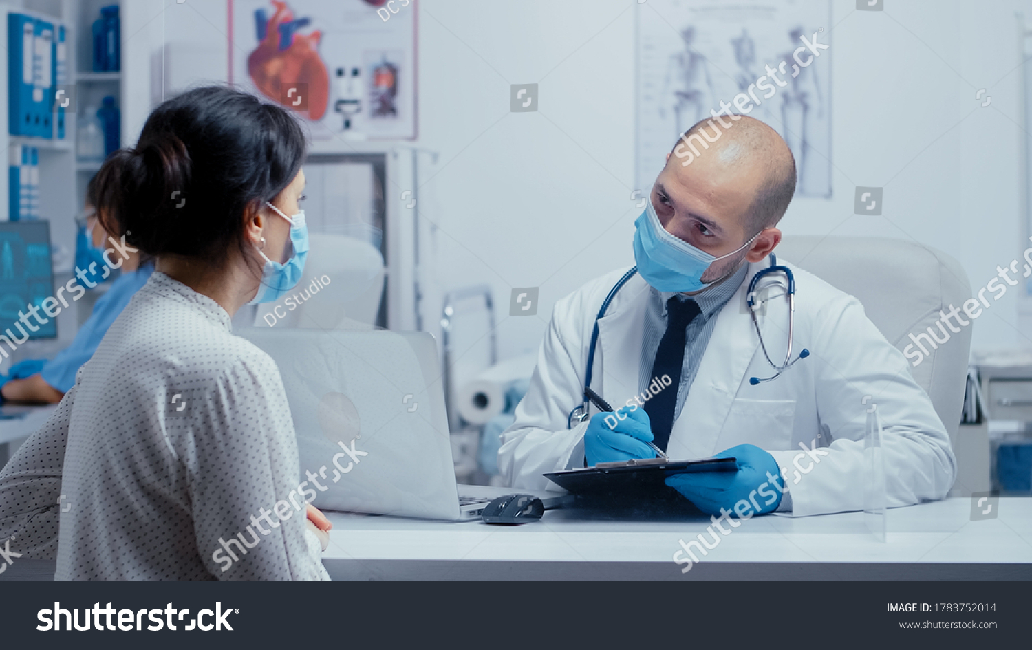 Doctor questioning patient during covid-19 pandemic, writing answears in clipboard. Medical consultation in protective equipment concept shot of sars-cov-2 global health pandemic crisis #1783752014