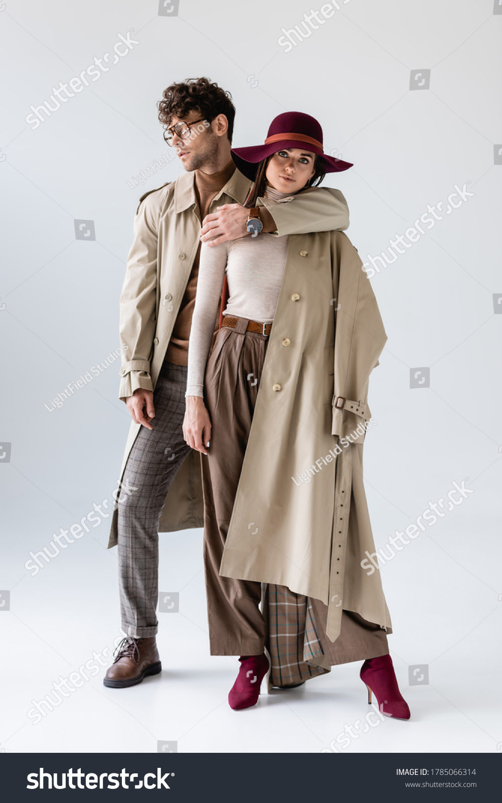 full length view of trendy man hugging stylish woman while posing in autumn clothes on grey #1785066314