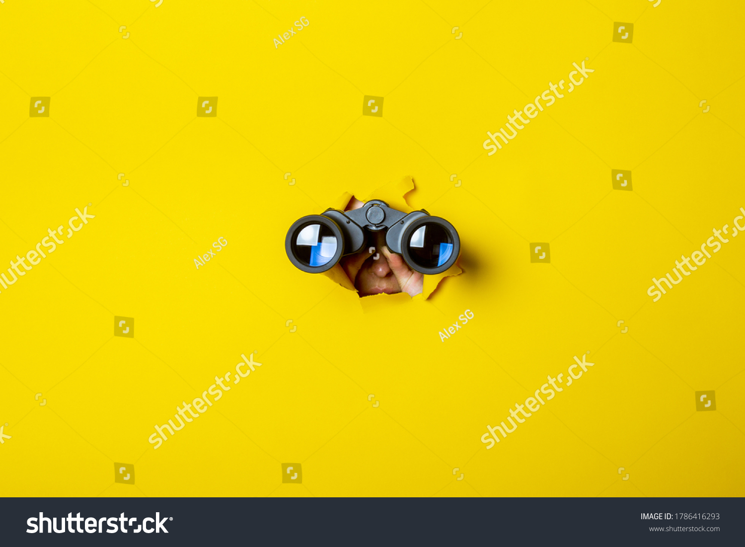 Female hand holds black binoculars on a yellow background. Journey, find and search concept #1786416293
