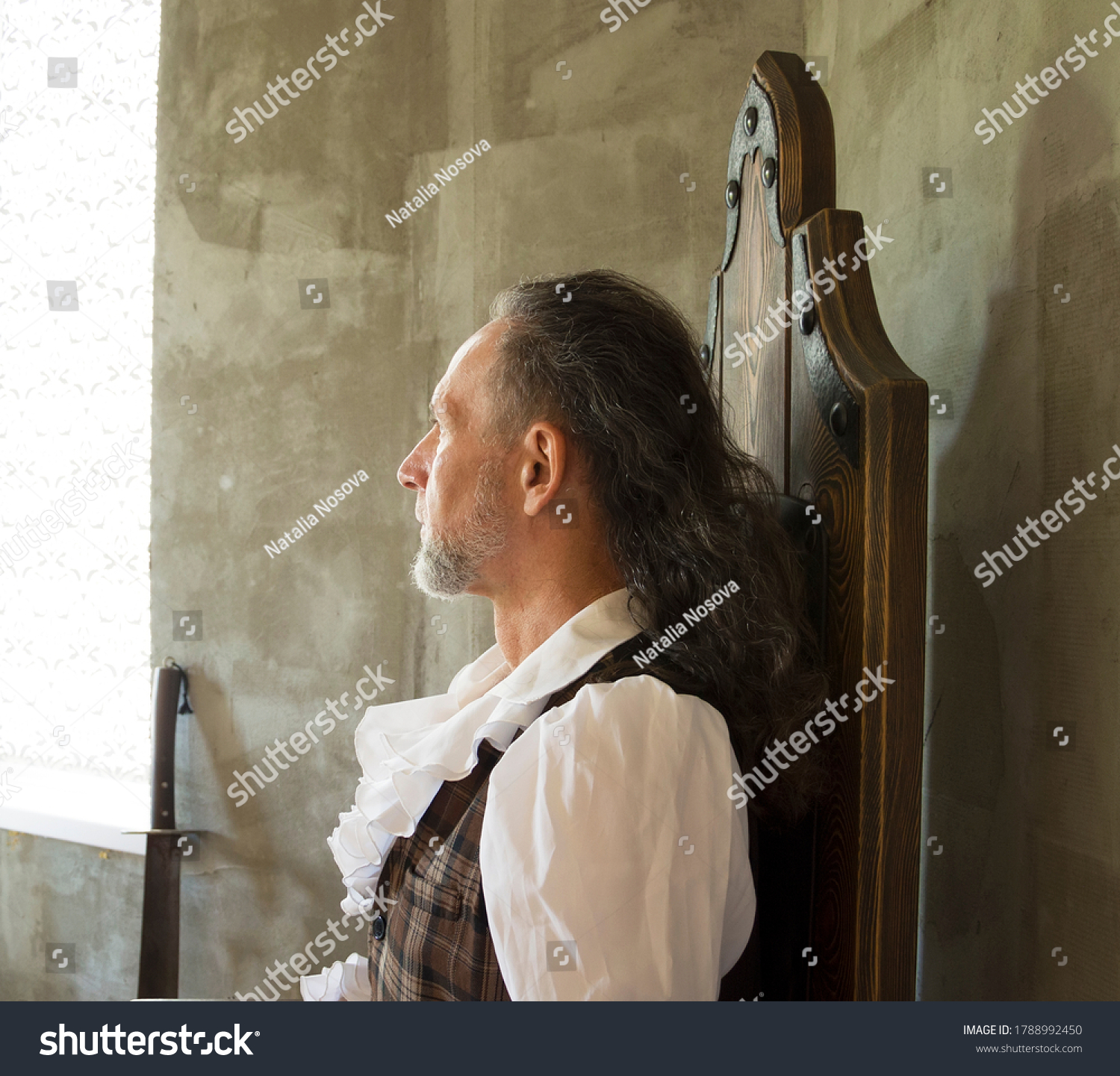 Portrait of a man with a beard in profile in vintage clothing, looking out the window on a gray background. Cosplay. #1788992450