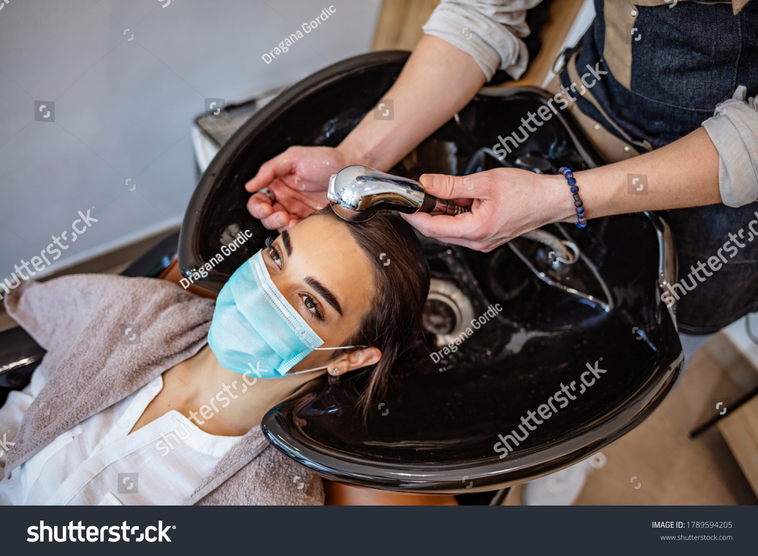 A young woman in a medical mask washes her hair in a barbershop during the covid-19 coronavirus pandemic. Reopening with security measures of Hairdressers in the Covid-19 pandemic #1789594205
