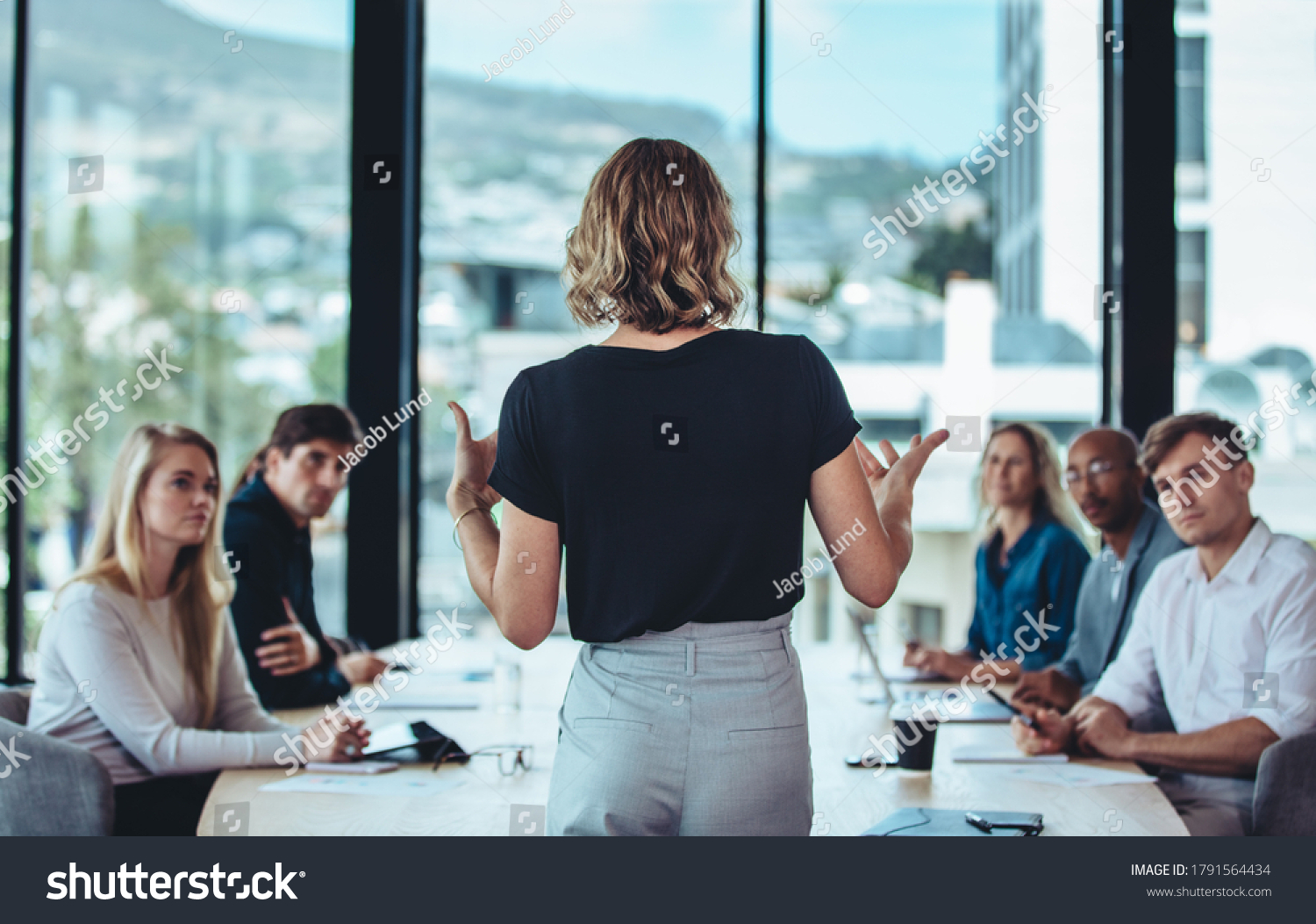 Rear view of a woman explaining new strategies to coworkers during conference meeting in office. Businesspeople meeting in office board room for new project discussion. #1791564434