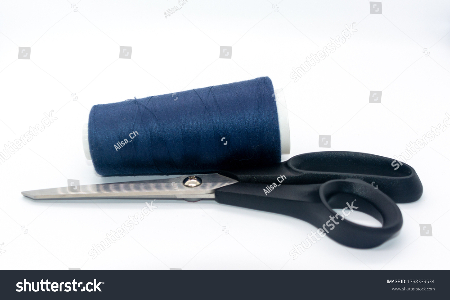 Blue bobbin thread and black scissors isolated on white background. Close up of a spool of blue sewing thread. Thread is a type of yarn but similarly used for sewing.  #1798339534