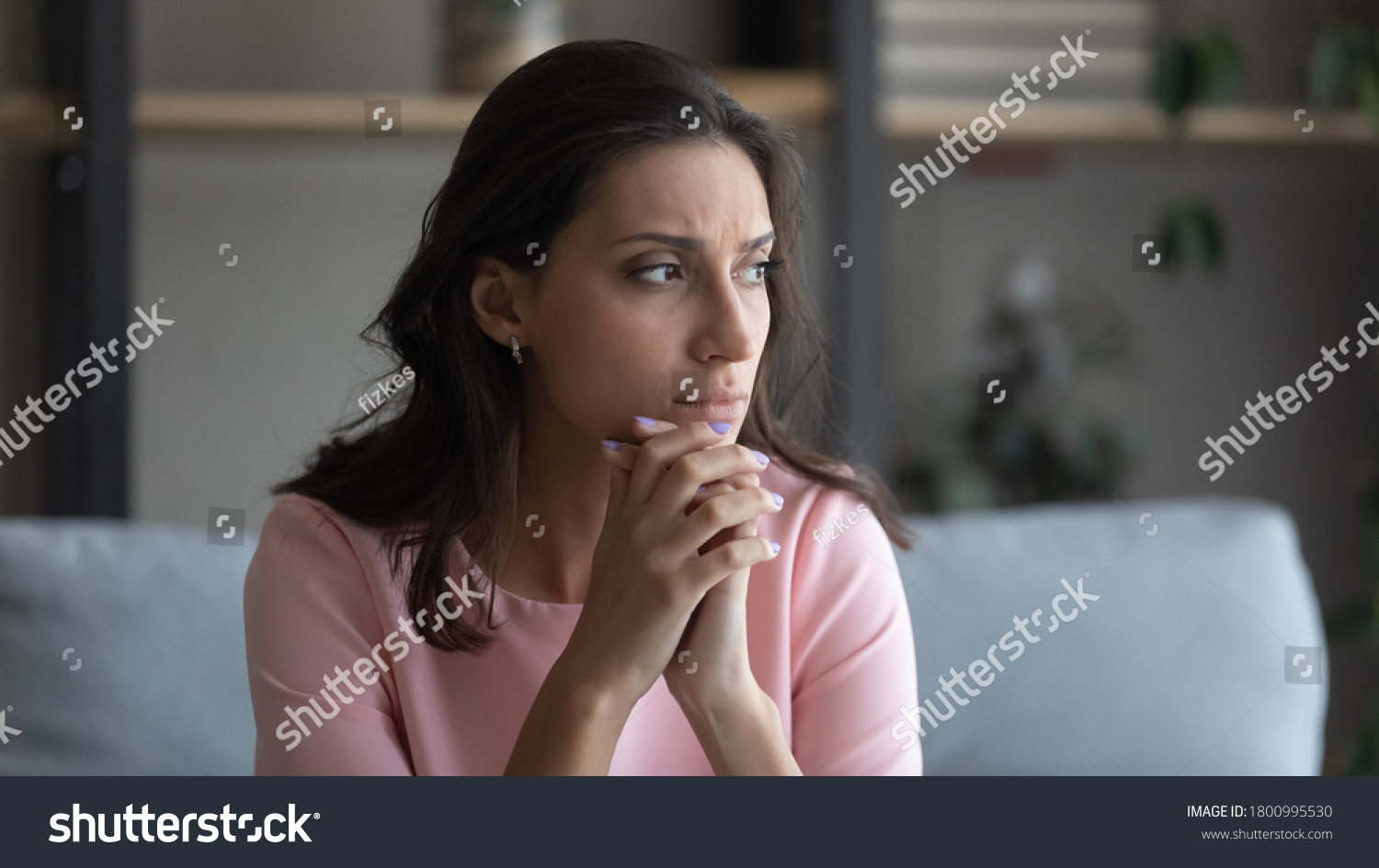 Worried young indian Arabic woman sit on couch at home look in distance thinking pondering, anxious unhappy arab mixed race female suffer from mental psychological personal problems, mourn or yearn #1800995530